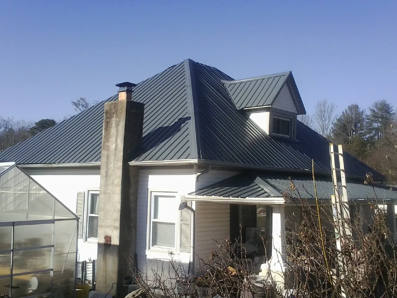 Dark blue standing seam metal roof on a white farmhouse with dormer — Slate & Tile Roof Repair by Roofing Brothers in Ambridge