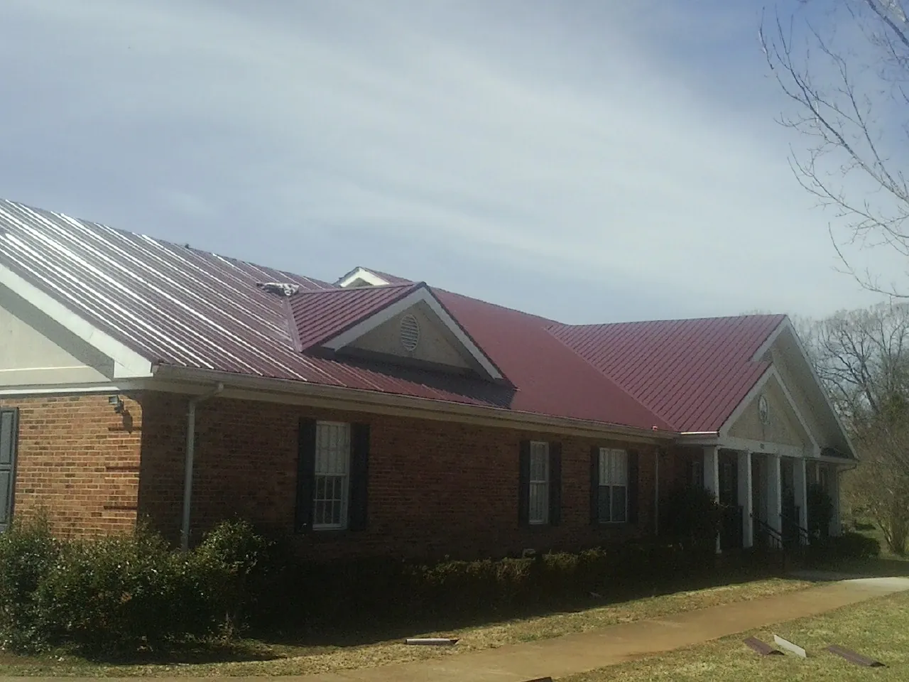 Red metal roof with gabled entries on a long brick building, from a Hail Damage Roof Repair job in Ambridge
