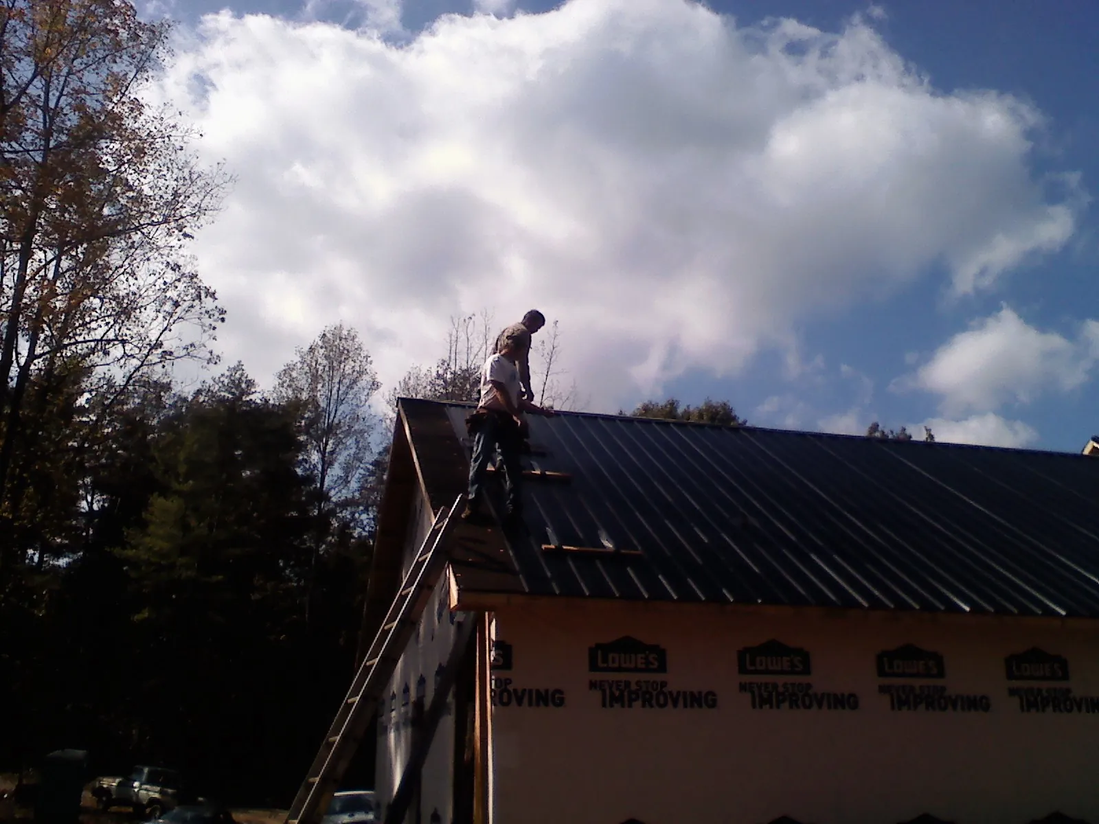 Roofer fastening dark metal panels high against a cloudy sky, from a Roof Inspection job in Ambridge