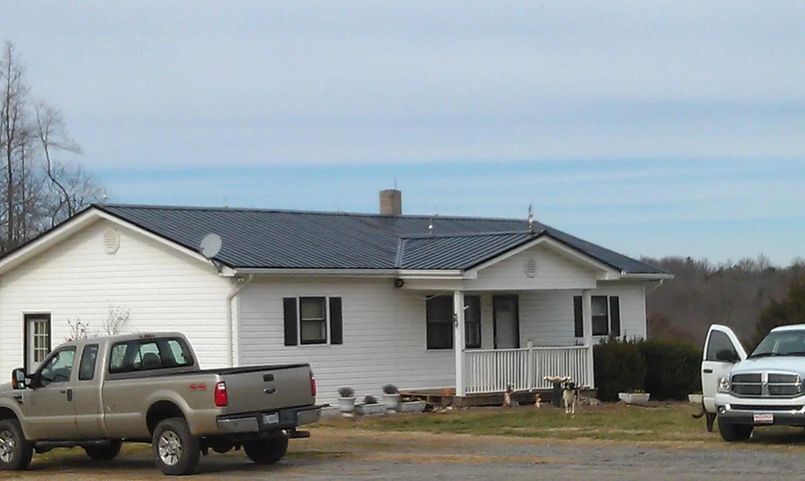 Finished dark metal roof on a white ranch home with work trucks parked in Ambridge