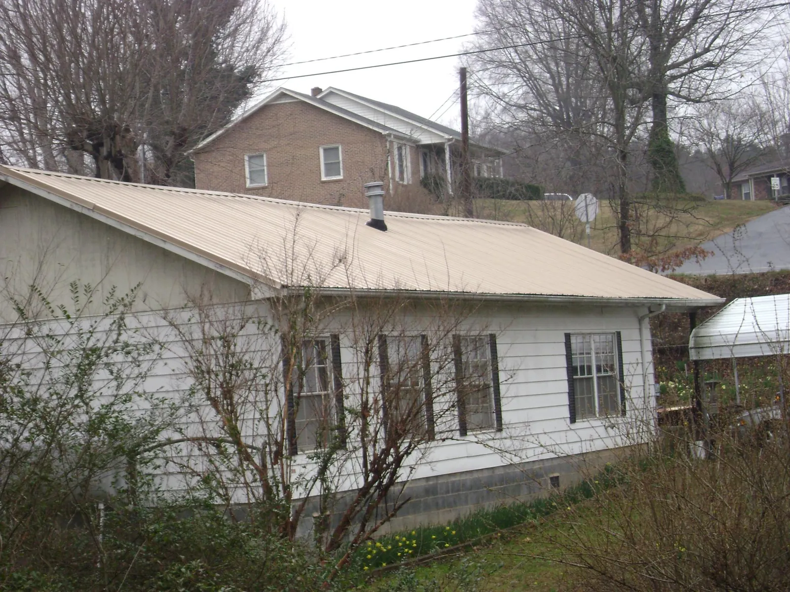Tan metal roof on a white sided house set into a hillside — Commercial Roofing by Roofing Brothers in Ambridge